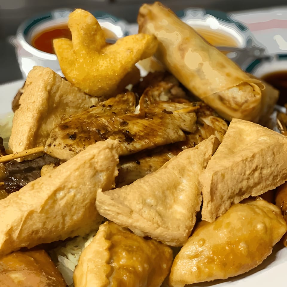 Close-up of a Thai appetizer platter with spring rolls, fried tofu, chicken satay, and dipping sauces.