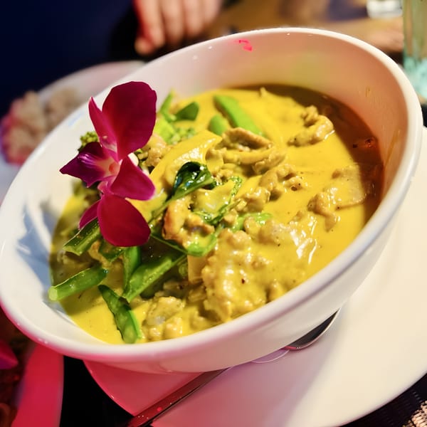 Close-up of Veranda Kitchen & Bar's yellow Thai curry with green vegetables and a purple orchid.